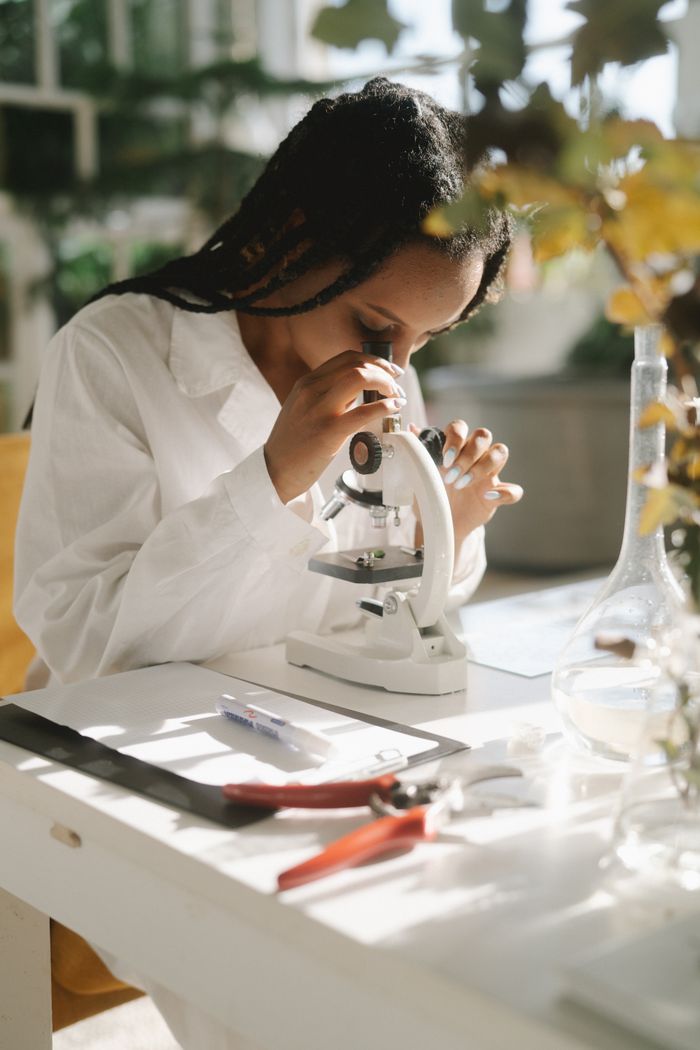 A female scientist in a lab coat uses a microscope in a well-lit laboratory setting.