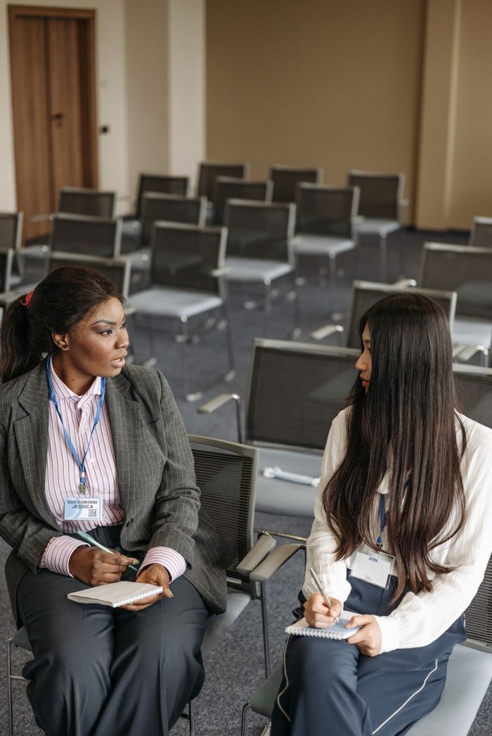 Two women engage in a discussion during a conference in a meeting room.