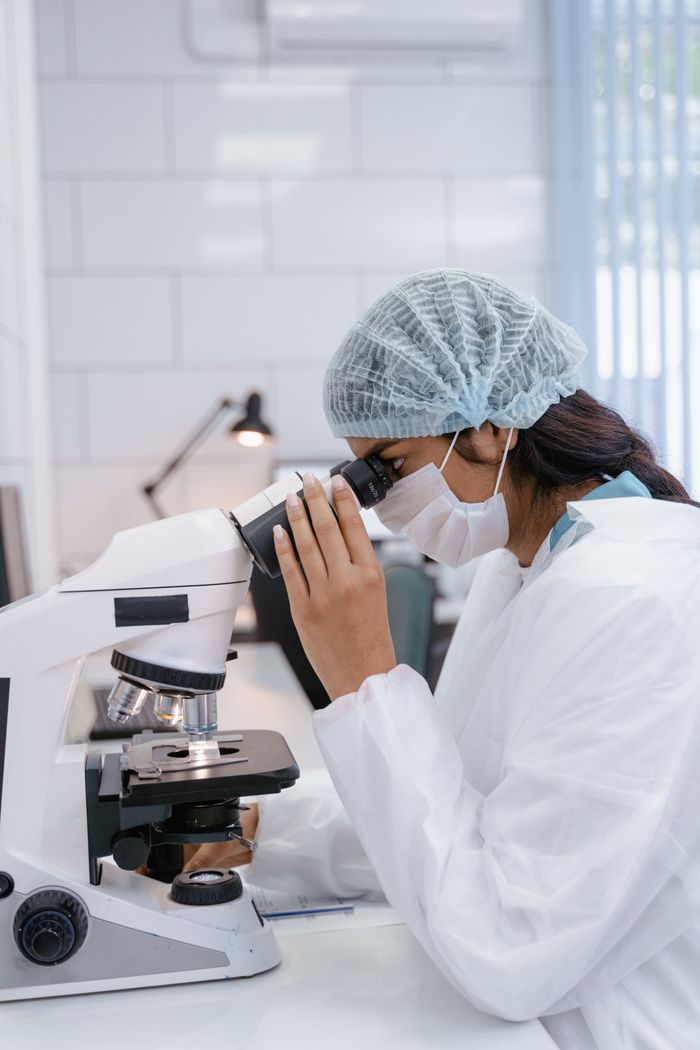 Female scientist in lab coat using microscope for research in a laboratory setting.