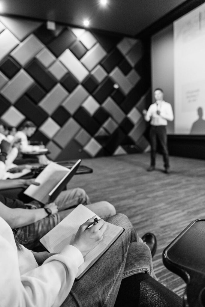 The Art of Drawing Readers In: Your attractive post title goes here Black and white shot of students taking notes during a lecture in a modern hall.