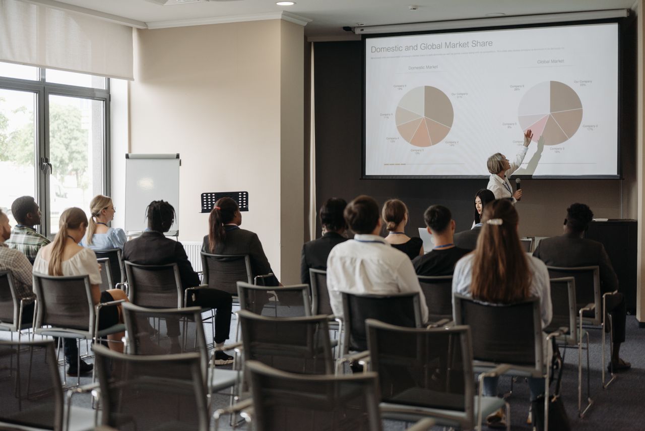 about-me Business professionals attending a seminar with a presentation on market share, highlighting diverse participation.